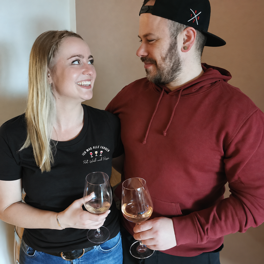 Digital bearbeitete eigene Paar-Trageansicht: Damen T-Shirt in Schwarz mit Ich mag alle Farben klein links auf der Brust; Begleitperson im neutralen Bordeaux-Hoodie.