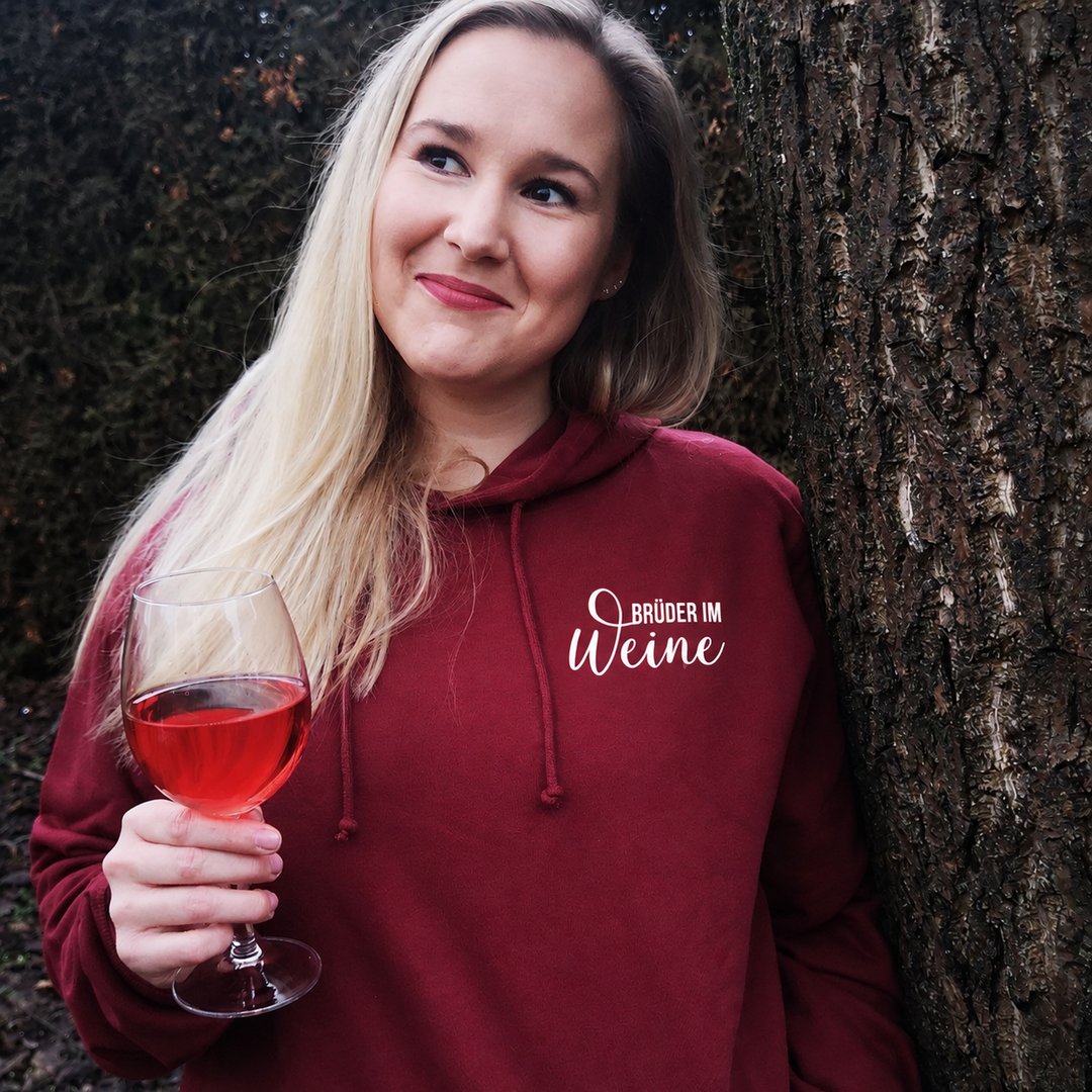 Bordeauxroter Brüder im Weine Hoodie mit kleinem weißem Brustmotiv, getragen draußen mit einem Weinglas.