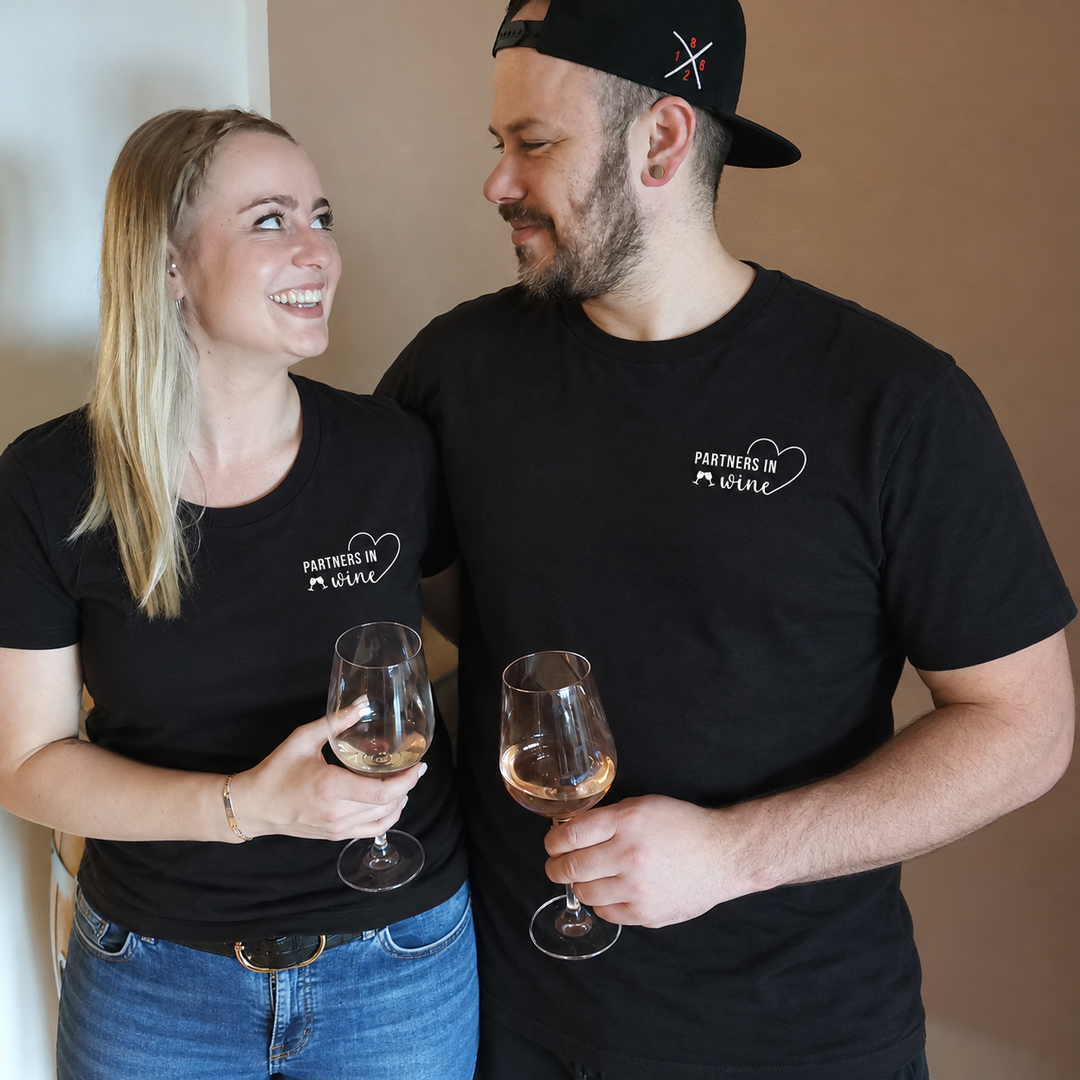 Digital bearbeitete eigene Paaraufnahme: Frau und Mann in schwarzen T-Shirts, beide mit kleinem weißen Partners in Wine Motiv links auf der Brust